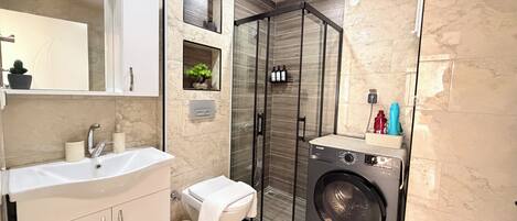A modern bathroom with a sink, mirror, toilet, shower, and a built-in washing machine.