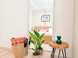 Une pièce comprenant un lit, un miroir, une plante verte, un panier en osier et une petite table en bois.