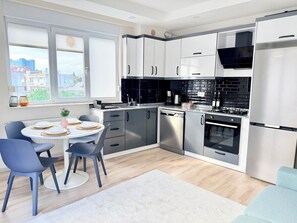 A modern kitchen with a dining area, featuring a round table with chairs, a built-in oven, and a dishwasher. - Modern Central Flat Near Old Town with Fast WiFi 2BR (ANTALYA)