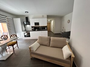 A compact living space with a kitchenette, a sofa, a dining table, and a chair. - Beautiful 3-Bedroom Apartment in the Village Center in a New Building (Solliès-Pont)