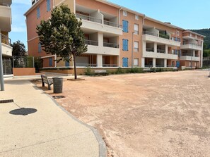 A multi-story residential building with balconies, a paved area with benches, and a tree. - Beautiful 3-Bedroom Apartment in the Village Center in a New Building (Solliès-Pont)