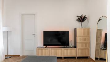 Una camera da letto con un letto, una TV su un mobile in legno, uno specchio e una lampada da terra.