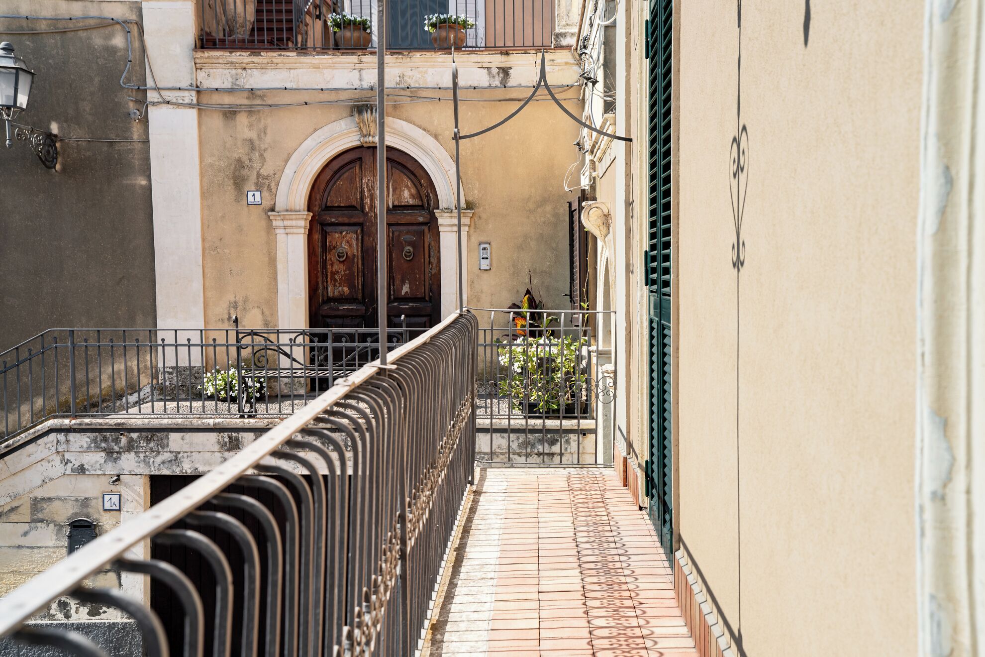 A narrow alleyway with a metal railing, a wooden door with an arched entrance, and a tiled floor.