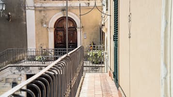 A narrow alleyway with a metal railing, a wooden door with an arched entrance, and a tiled floor.