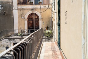 Une ruelle étroite, bordée d’une rambarde en métal, avec une porte en bois dotée d’un portail en arc de cercle et un sol carrelé.