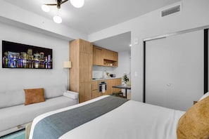 A modern hotel room with a bed, a sofa, a kitchenette, and a cityscape view. - Luxury Studio | Pool, Gym & Prime Location (Miami)