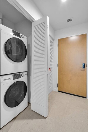 A laundry room with two stacked front-loading washing machines and a closed wooden door. - Luxury Studio | Pool, Gym & Prime Location (Miami)