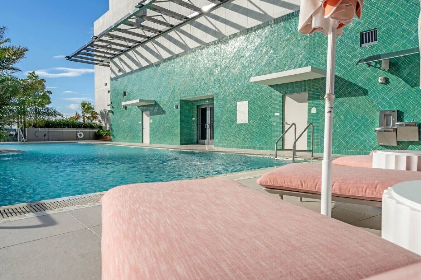 Una piscina con sillas de descanso y un edificio con fachada de azulejos verdes.