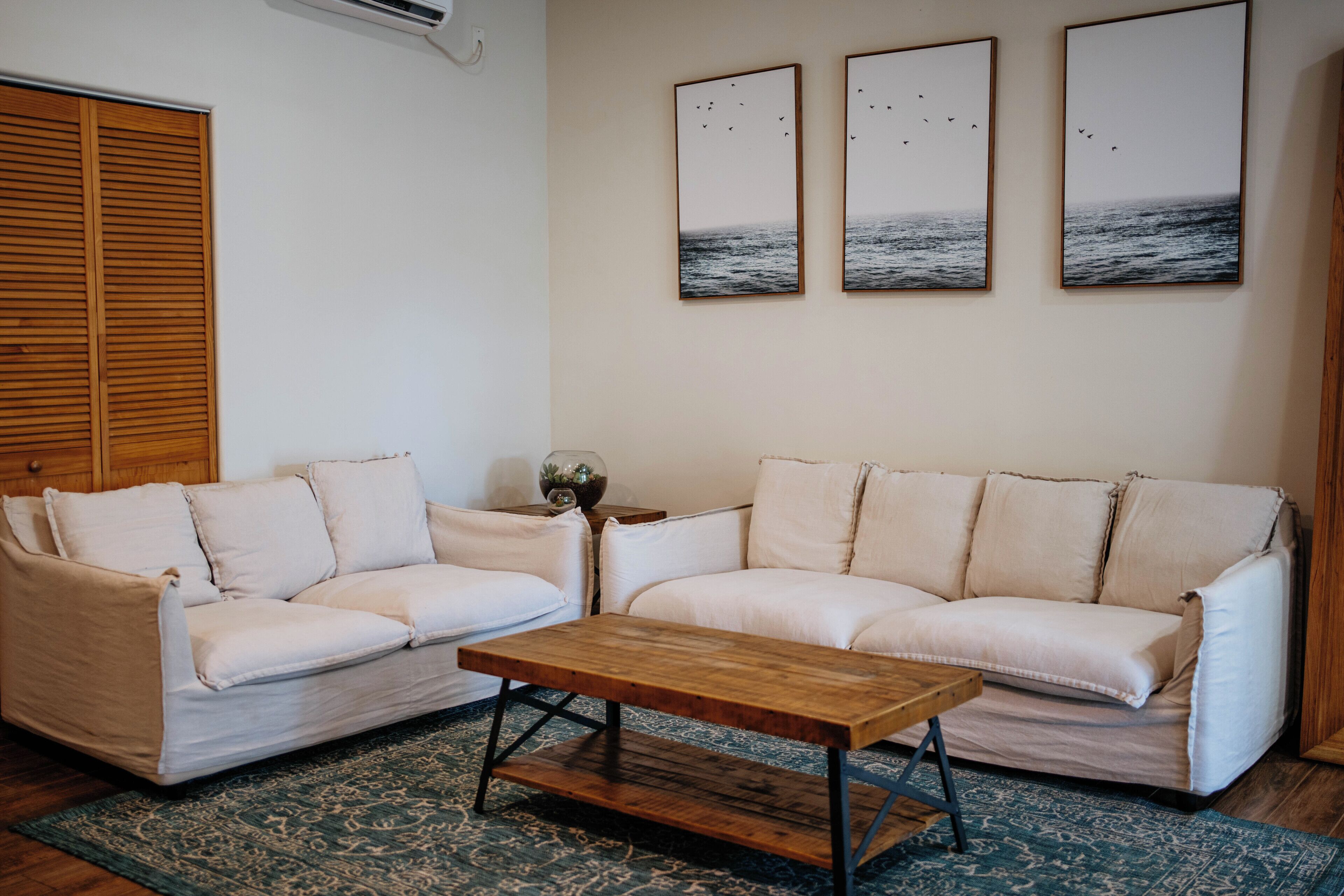 A living room with a beige sofa, a wooden coffee table, and three framed pictures on the wall.