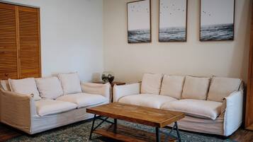 A living room with a beige sofa, a wooden coffee table, and three framed pictures on the wall.