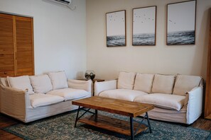 A living room with a beige sofa, a wooden coffee table, and three framed pictures on the wall. - A gorgeous 2-bedroom, 2-bath apartment in the center of Playa Venao (Las Escobas del Venado)