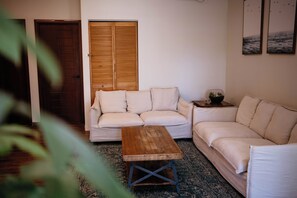 A living room with a wooden door, a white sofa, a wooden coffee table, and a patterned rug.