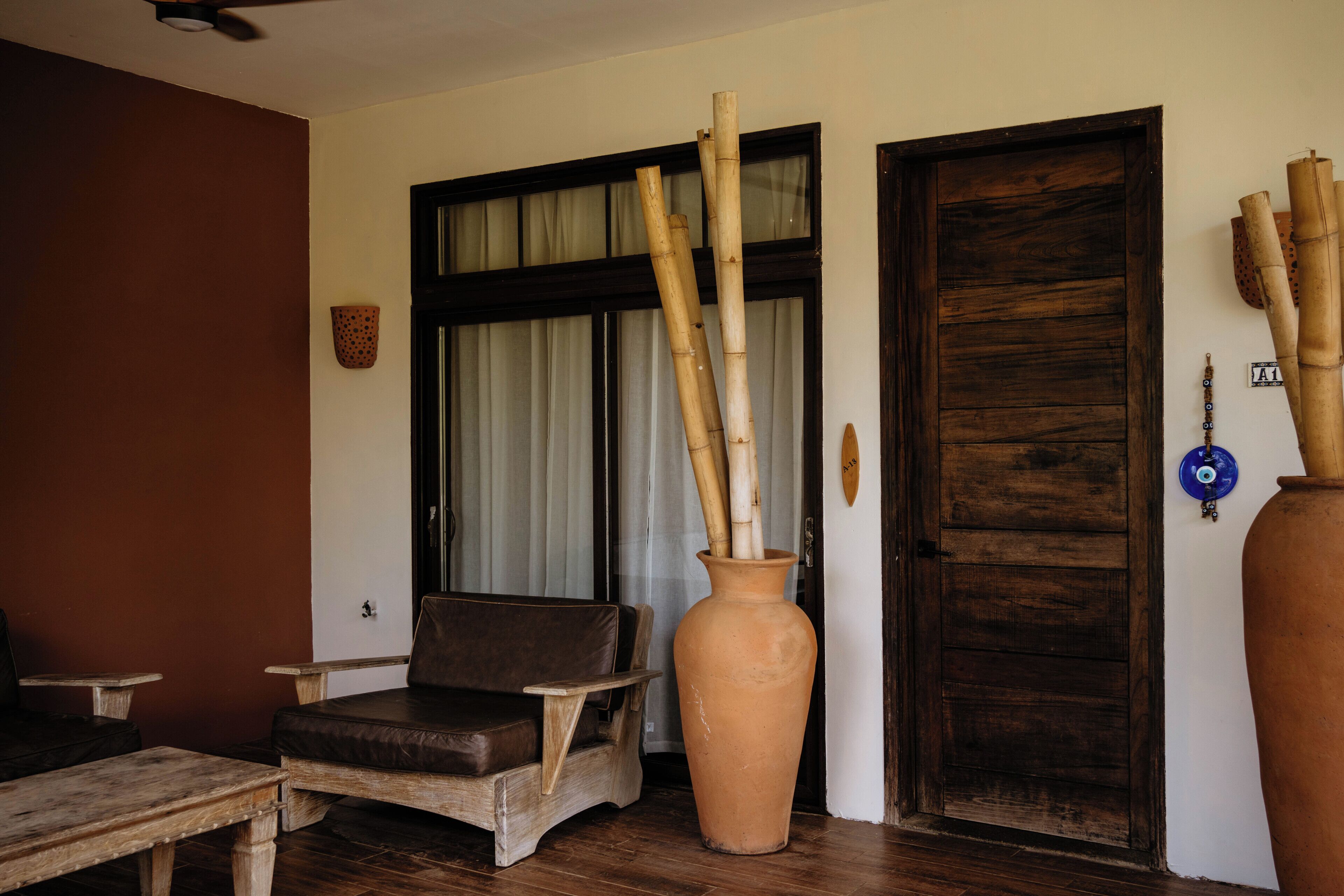 A room with a wooden bench, a large terracotta vase, and a wooden door.
