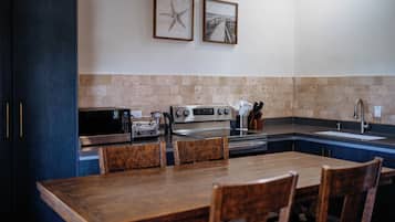 A kitchen with a dining table, chairs, a microwave, a toaster, a stove, and a sink.