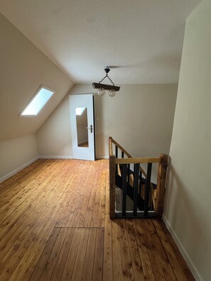 A room with wooden flooring, a sloped ceiling, a door, and a small window.