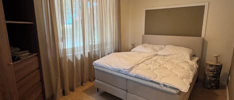 A bedroom with a bed, wooden floor, a wardrobe, and a window with curtains.