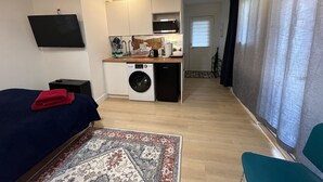 A compact living space with a bed, a washing machine, a kitchenette, and a TV.