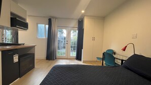 A bedroom with a bed, a desk, a chair, a wardrobe, and a kitchenette.