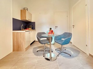 Une cuisine compacte avec un coin repas, comprenant une table ronde avec deux chaises et un saladier de fruits.