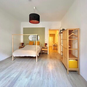 A bedroom with a four-poster bed, a bedside table, a hanging lamp, and a wooden wardrobe with shelves. - Servus Homes - Metro Stadthalle - Amadeus (Vienna)
