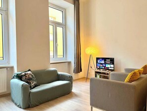 A living room with a sofa, a chair, a floor lamp, and a television. - Servus Homes - Metro Stadthalle - Amadeus (Vienna)