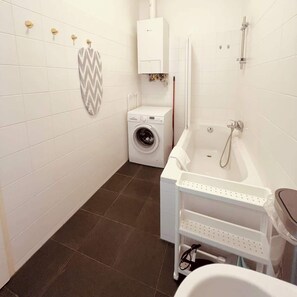 A compact bathroom with a washing machine, a bathtub, and a shower. - Servus Homes - Metro Stadthalle - Amadeus (Vienna)