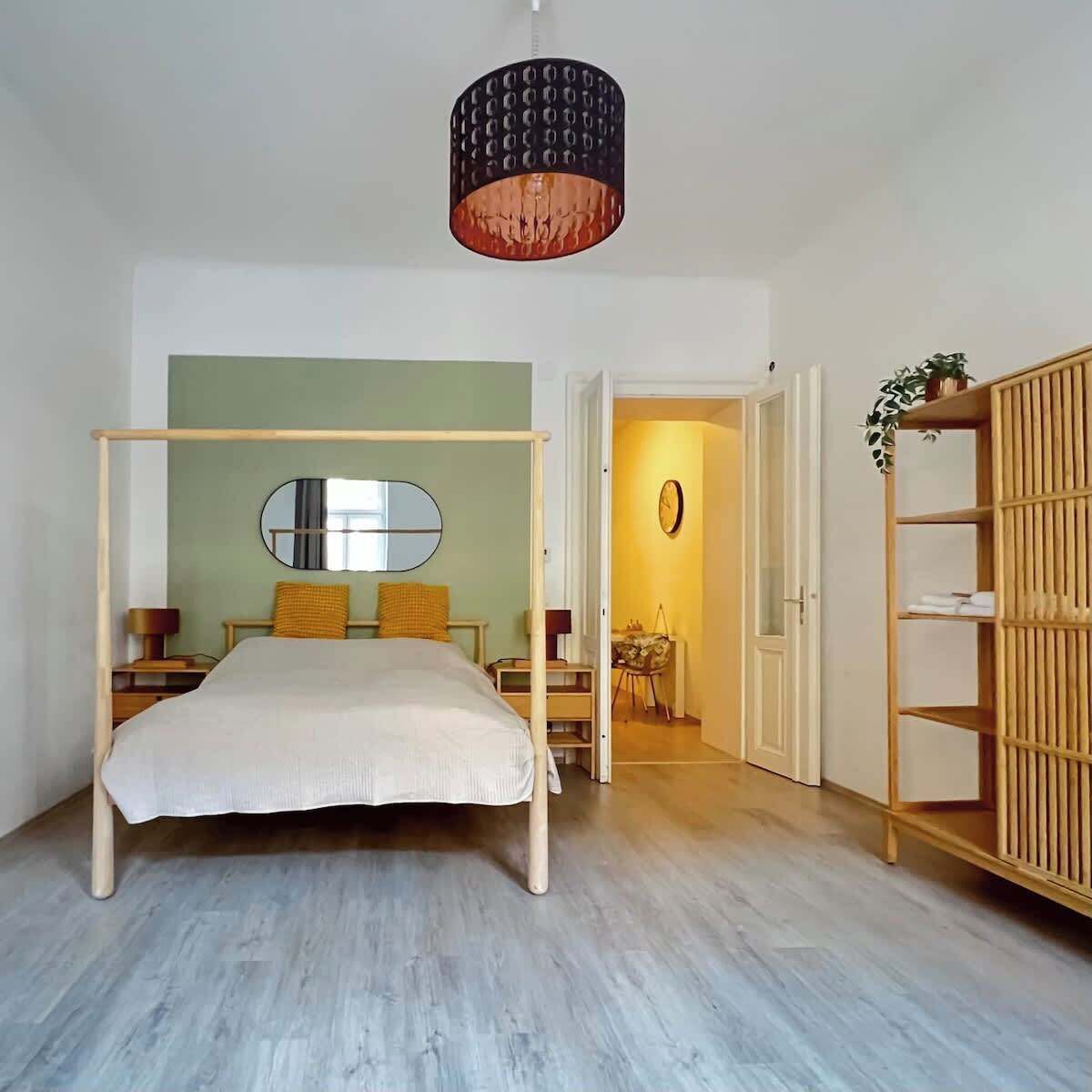 Een slaapkamer met hemelbed, een houten garderobe, een spiegel en een hanglamp.