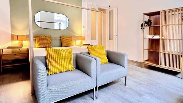 A modern living room with a sofa, a mirror, a wooden bookshelf, and a lamp. - Servus Homes - Metro Stadthalle - SISSI (Wien)
