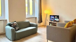 A living room with a sofa, armchair, and a television on a stand. - Servus Homes - Metro Stadthalle - SISSI (Wien)