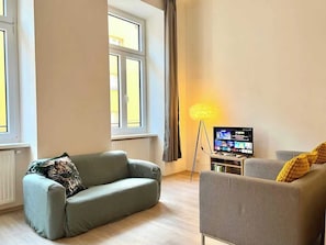 A living room with a sofa, armchair, and a television on a stand. - Servus Homes - Metro Stadthalle - SISSI (Wien)