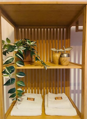 A wooden shelf unit with two levels, one holding a plant and decorative items, and the other with folded towels. - Servus Homes - Metro Stadthalle - SISSI (Wien)