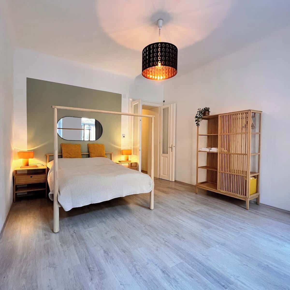 Quarto com cama de dossel, abajures, guarda-roupa de madeira e luminária pendente.