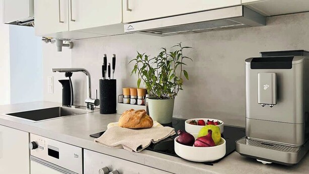 Une cuisine moderne équipée d’un four encastré, d’une machine à café et d’une plante en pot.