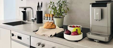 A modern kitchen with a built-in oven, a coffee machine, and a potted plant.