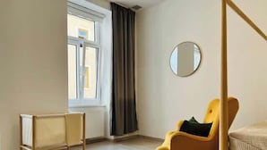 Une pièce comprenant un lit, une chaise, une fenêtre, un radiateur et un miroir.