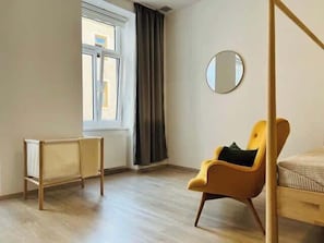 Ein Zimmer mit einem Bett, einem Sessel, einem Fenster, einer Heizung und einem Spiegel.