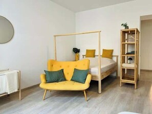 Um quarto com um sofá amarelo, uma cama, uma estante de madeira e um espelho redondo na parede.