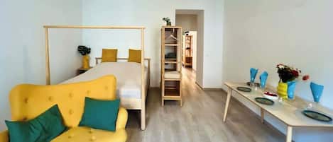 A room with a yellow sofa, a bed with a wooden frame, a wooden ladder, and a table with plates and glasses.