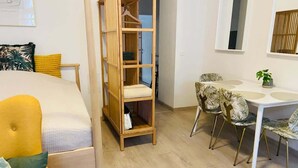 Une pièce comprenant un lit, une armoire en bois, une table à manger avec des chaises et une petite plante en pot.