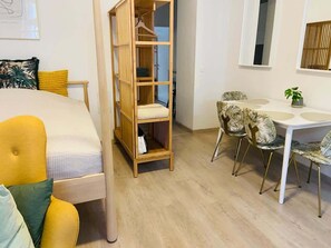 Ein Zimmer mit einem Bett, einem Holzschrank, einem Esstisch mit Stühlen und einer kleinen Topfpflanze.