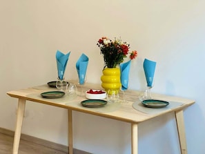 Ein Esstisch mit blauen Servietten, einer gelben Vase mit Blumen und einer Obstschale.