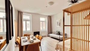 A modern room with a dining table, sofa, and a wooden bed frame. - SOUND OF MUSIC · Servus Homes – Metro Stadthalle – Sound Of Music (Vienna)
