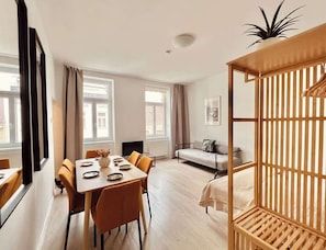 A modern room with a dining table, sofa, and a wooden bed frame. - SOUND OF MUSIC · Servus Homes – Metro Stadthalle – Sound Of Music (Vienna)