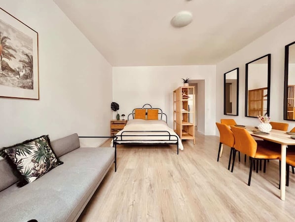 Een moderne slaapkamer met een bed, een bank, een eettafel met stoelen en een boekenkast.