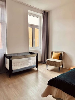 Een kamer met een stapelbed, een stoel met kussen, een raam met gordijnen en een radiator.