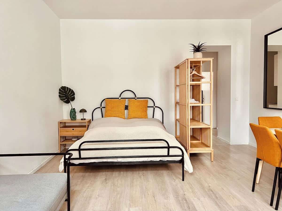 A bedroom with a bed, a nightstand, a wooden wardrobe, and a chair.