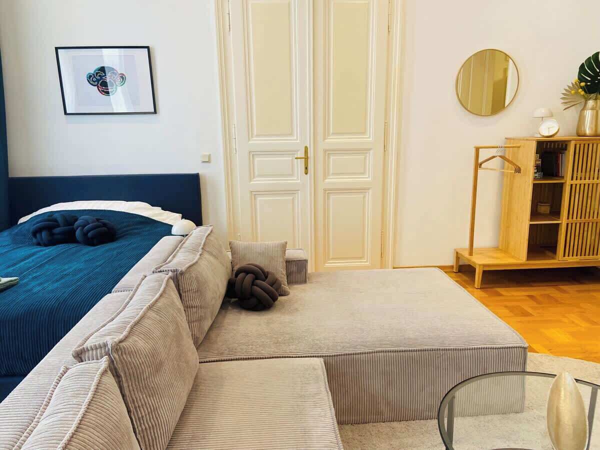 A bedroom with a bed, a sofa, a bedside table, a mirror, and a wardrobe.
