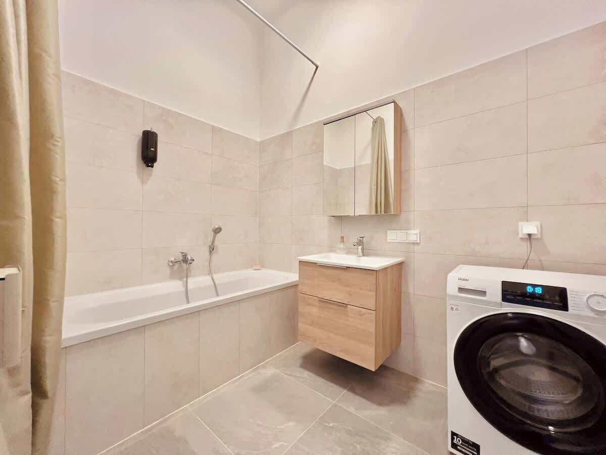A modern bathroom with a bathtub, a wooden vanity, and a front-loading washing machine.