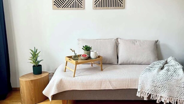 Ein Zimmer mit einem Bett, einem Nachttisch mit Pflanze, einem Tablett mit Schüssel und Tasse sowie einer Wand mit geometrischer Wandkunst.