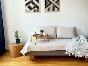A room with a bed, a bedside table with a plant, a tray with a bowl and mug, and a wall with geometric wall art. - Servus Homes - Metro Stadthalle - FRANZ (Wien)